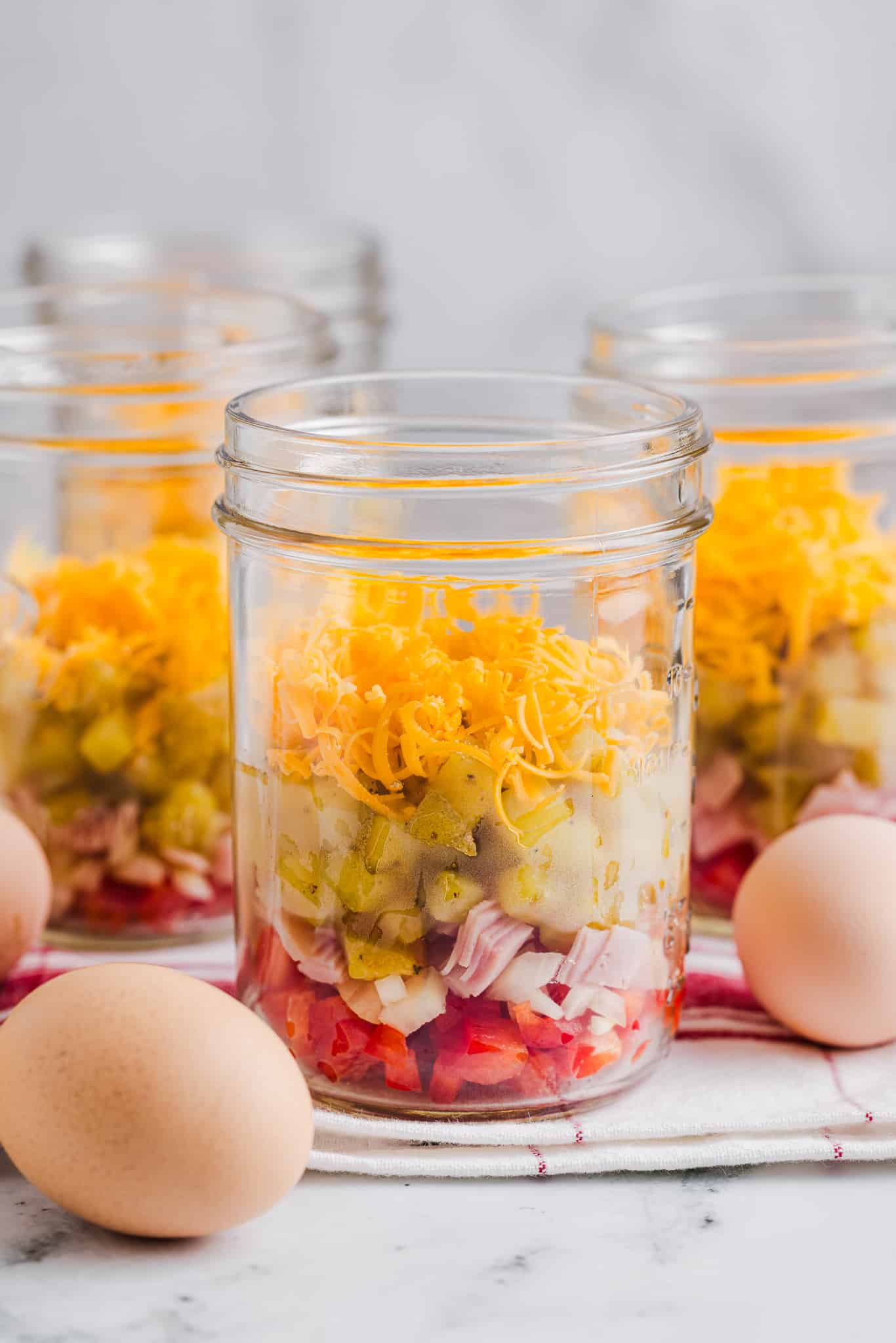 Mason jar layered with red bell pepper, onion, ham, roasted potatoes and cheese.