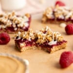 No bake PB and J oat bars sliced on parchment paper with a bite taken out of one.