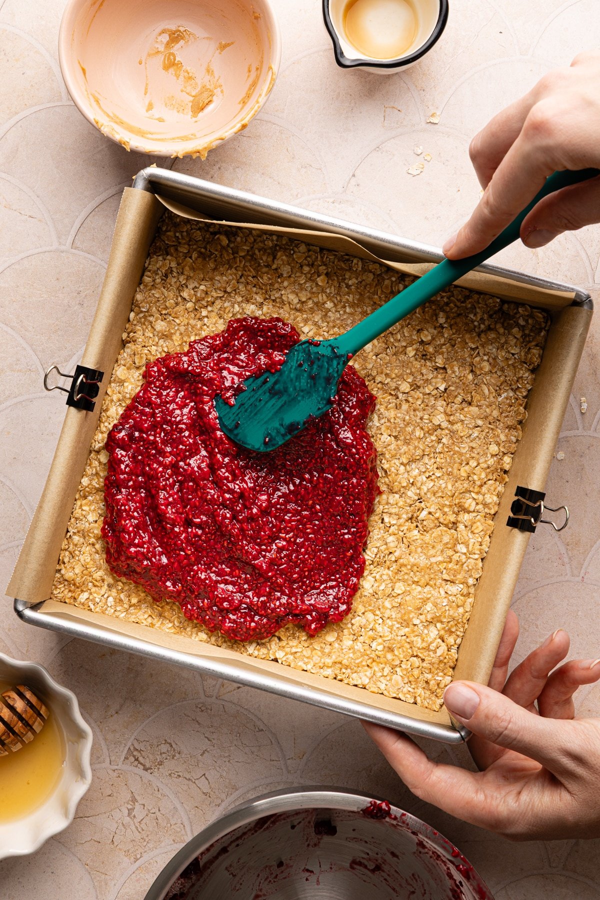 Raspberry chia jam being spread on top of a peanut butter oat layer for no bake PB and J oat bars.
