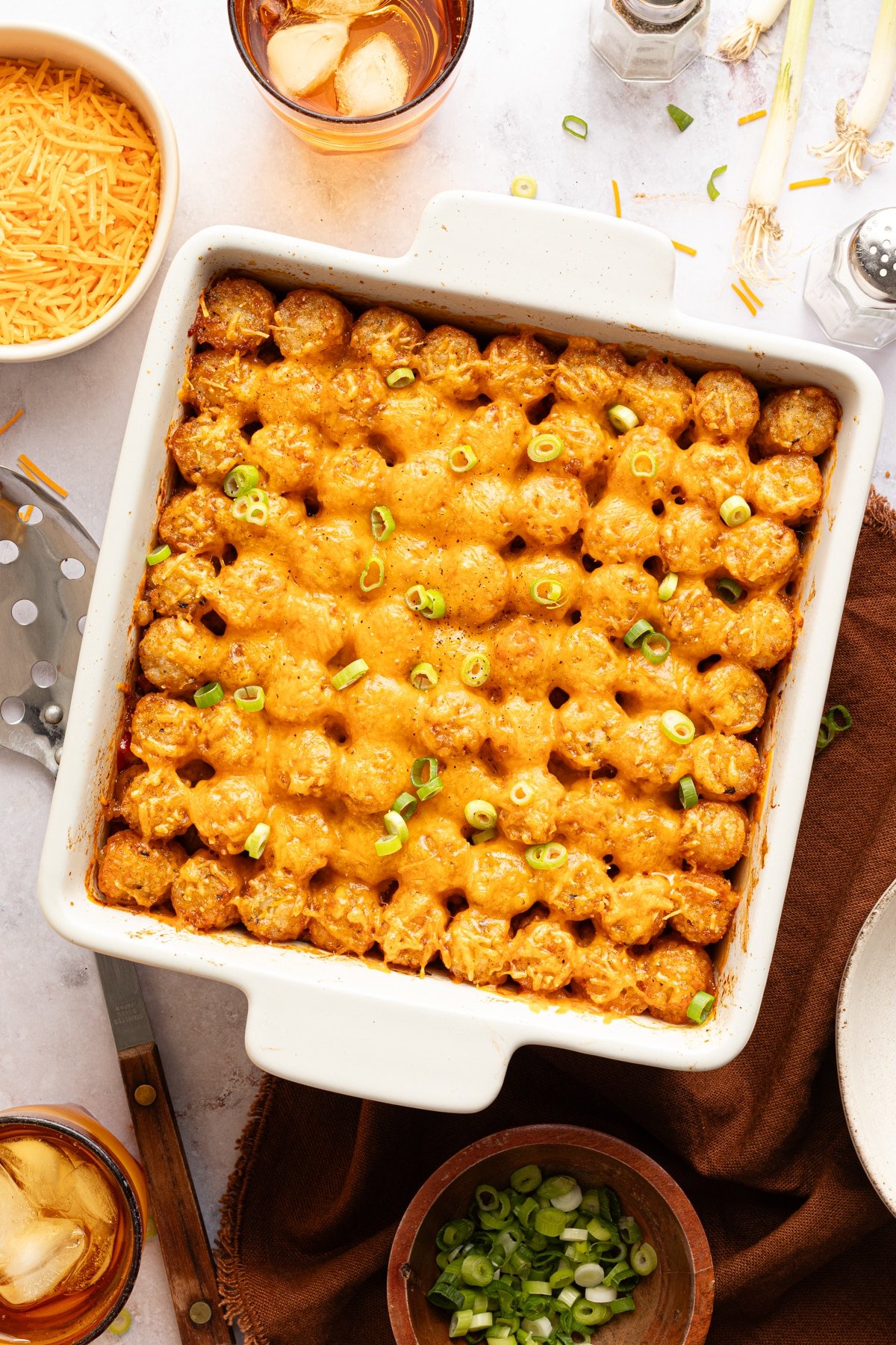 Sloppy joe tater tot casserole in a square white baking dish from the oven topped with melted cheese and sliced scallions.