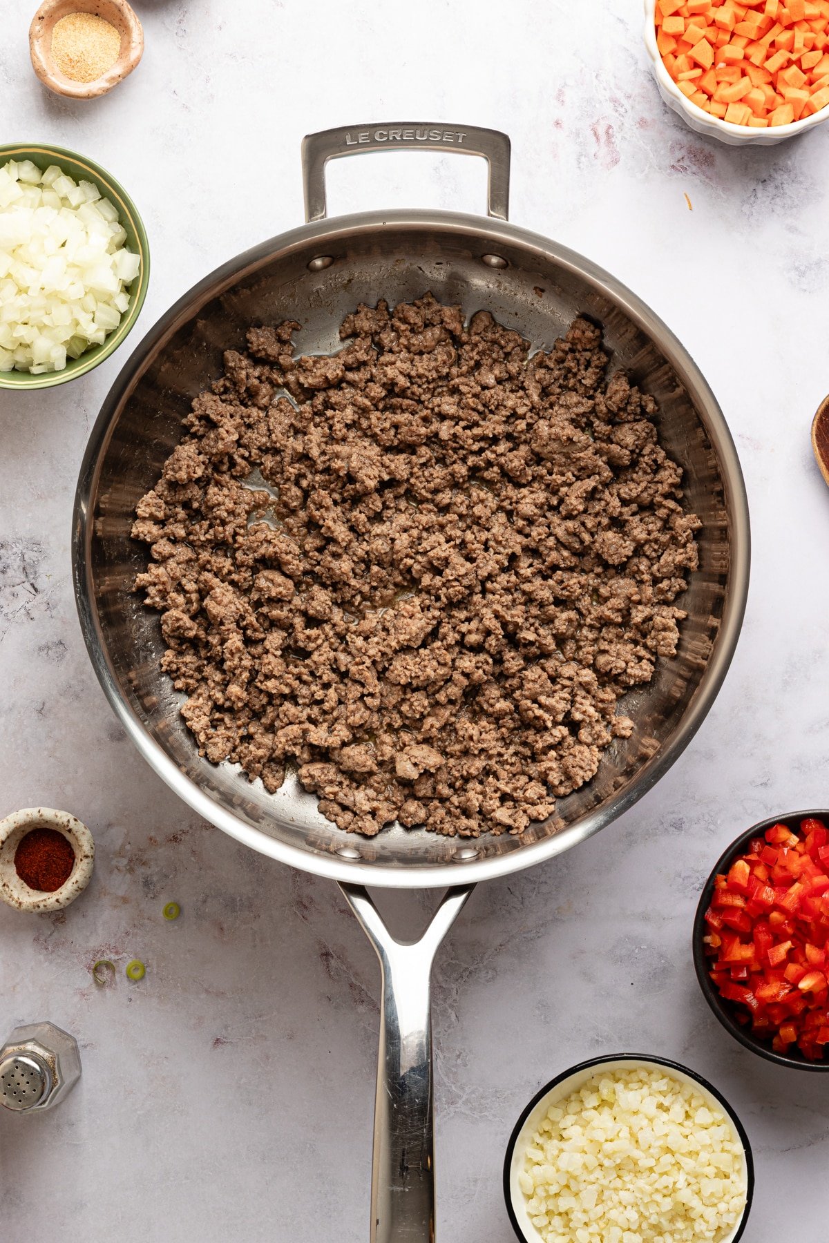 Cooked ground beef broken apart in a large stainless steel skillet.