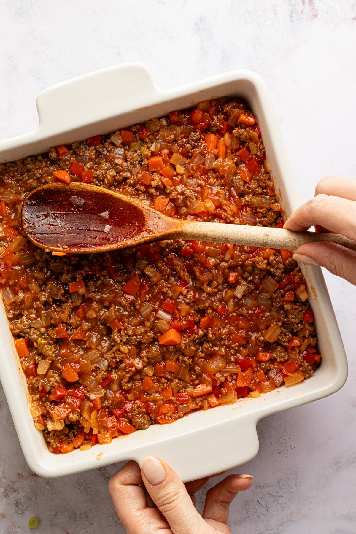Filling for sloppy joe tater tot casserole being smoothed into a baking dish with a wooden spoon.