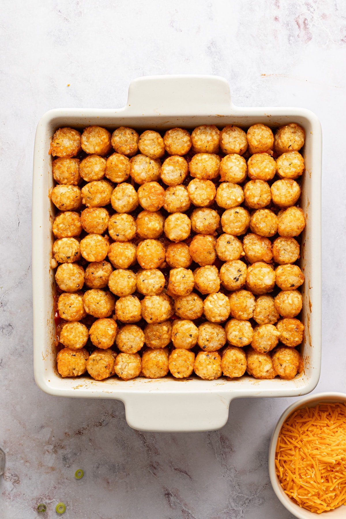A square baking dish lined with tater tots for sloppy joe tater tot casserole.