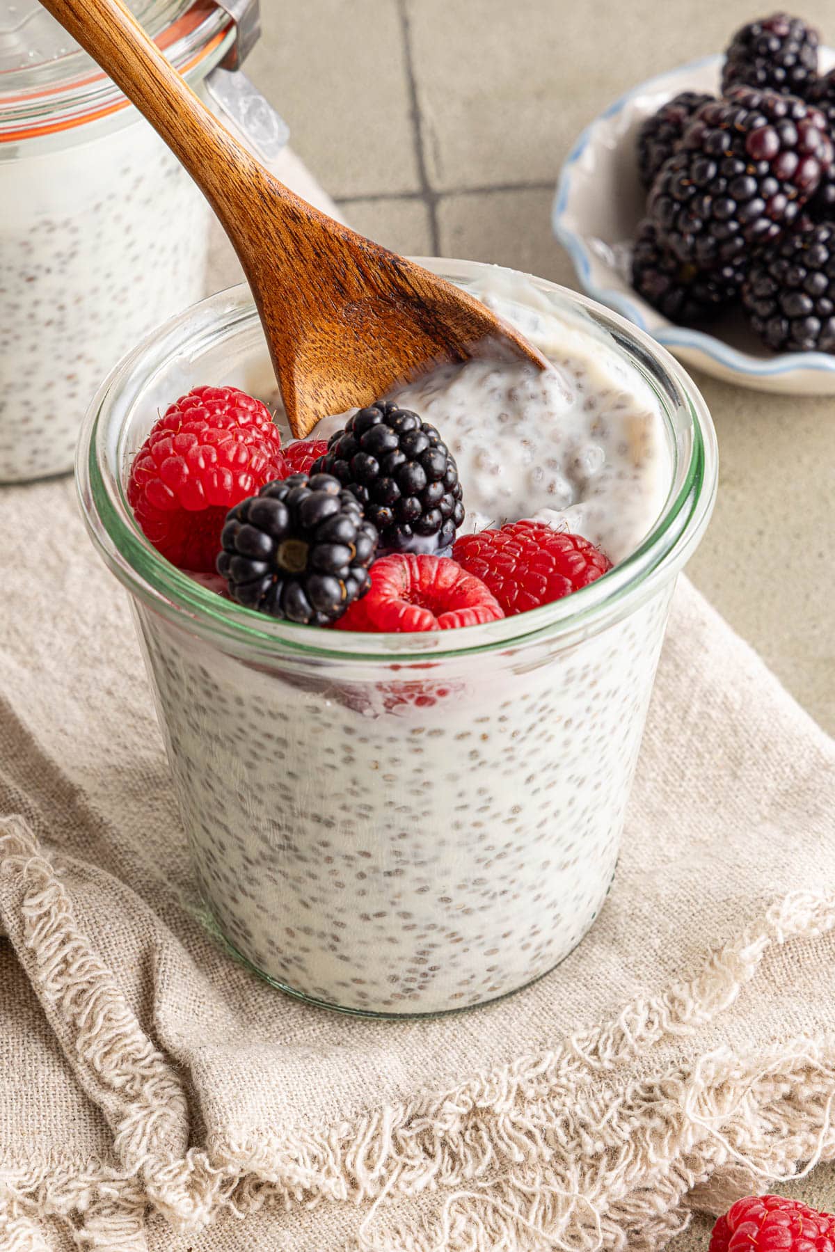 A small wooden spoon scoops some kefir chia pudding out of a glass container.