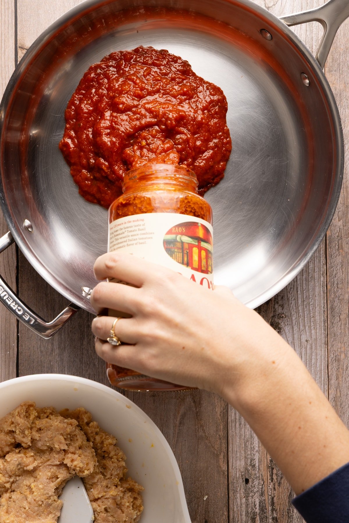 Tomato sauce being poured into a pan for chicken parm meatballs.