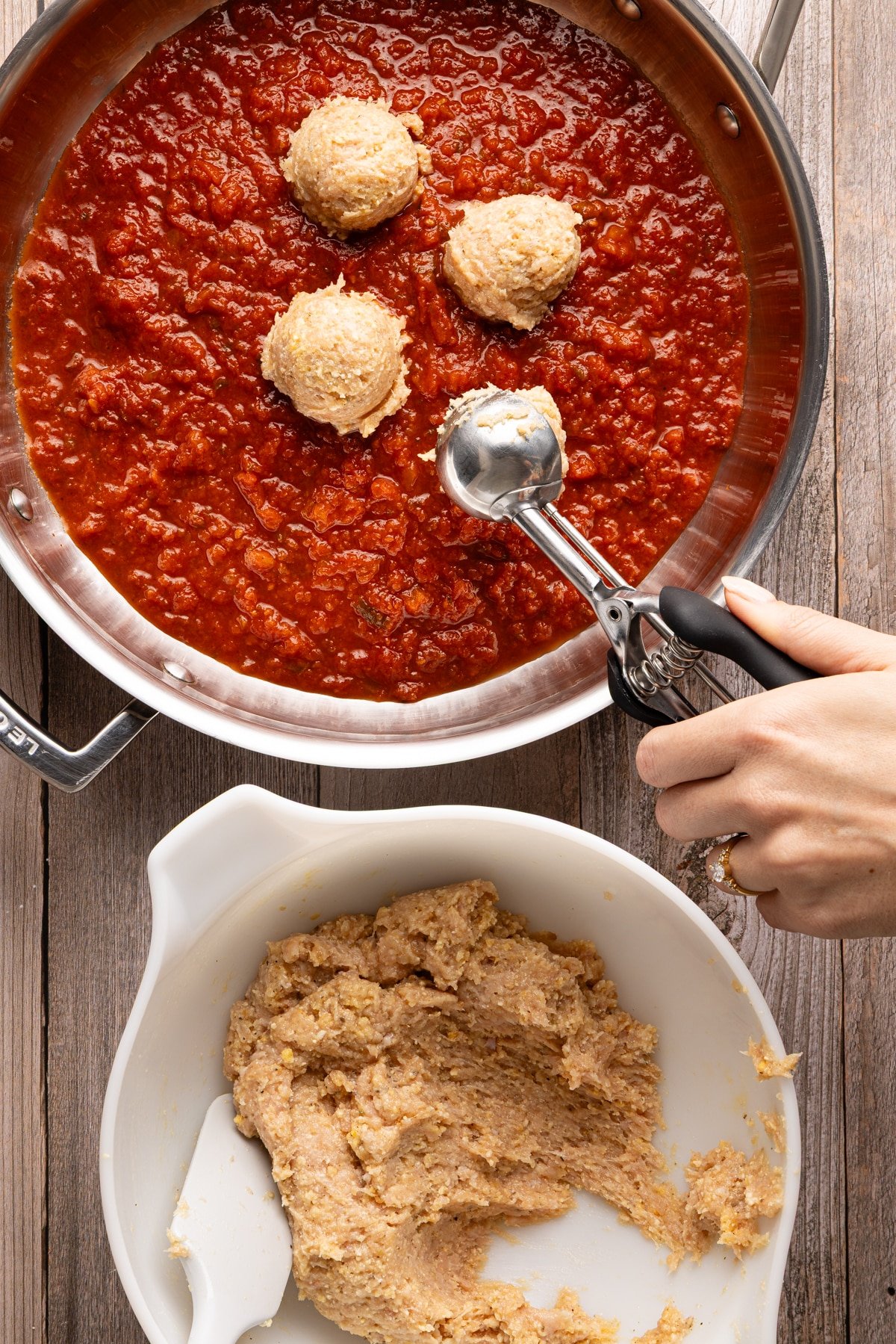 Chicken meatballs being scooped into skillet with tomato sauce.