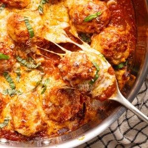 A pan of chicken parmesan meatballs with a cheesy meatball being scooped out of the pan.