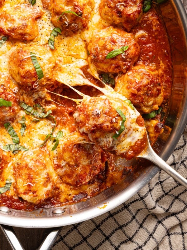 A pan of chicken parmesan meatballs with a cheesy meatball being scooped out of the pan.