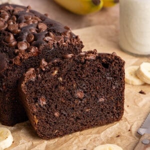 One slice of double chocolate banana bread leans on the remaining loaf on a brown piece of parchment paper.