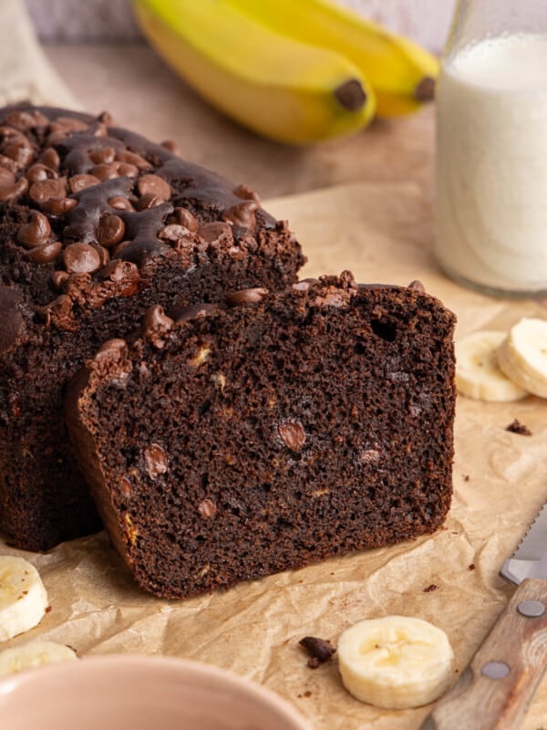One slice of double chocolate banana bread leans on the remaining loaf on a brown piece of parchment paper.