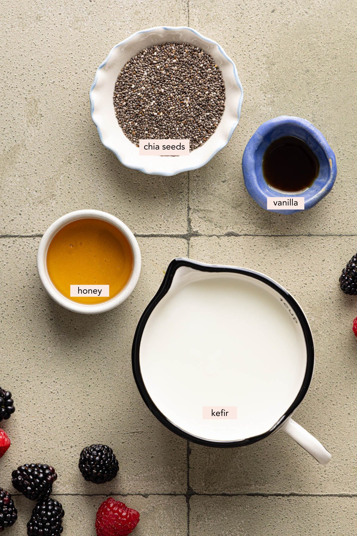 All of the ingredients you need to make Kefir chia pudding in bowls on a countertop including kefir, chia seeds, honey, and vanilla.