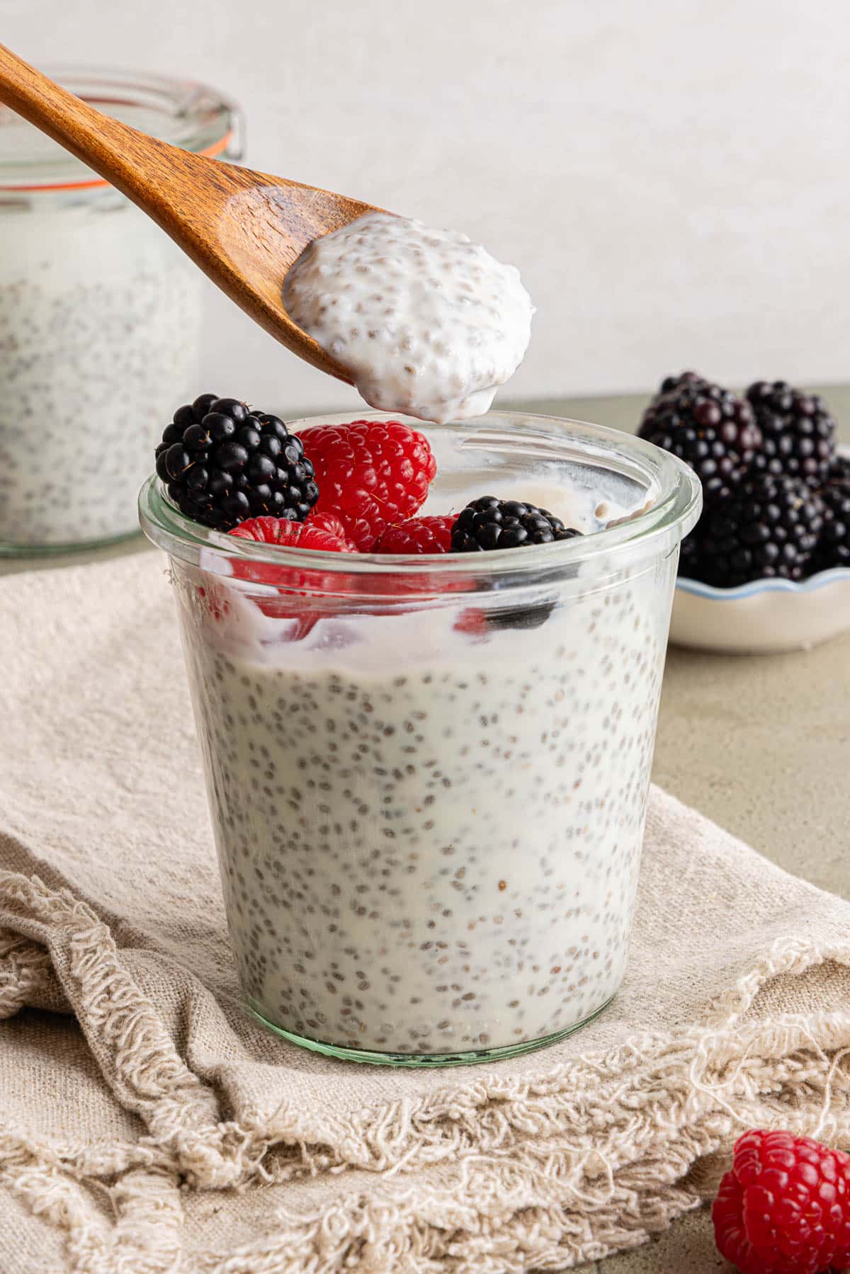 A spoon with kefir chia pudding on it sits over a jar of the pudding and berries.