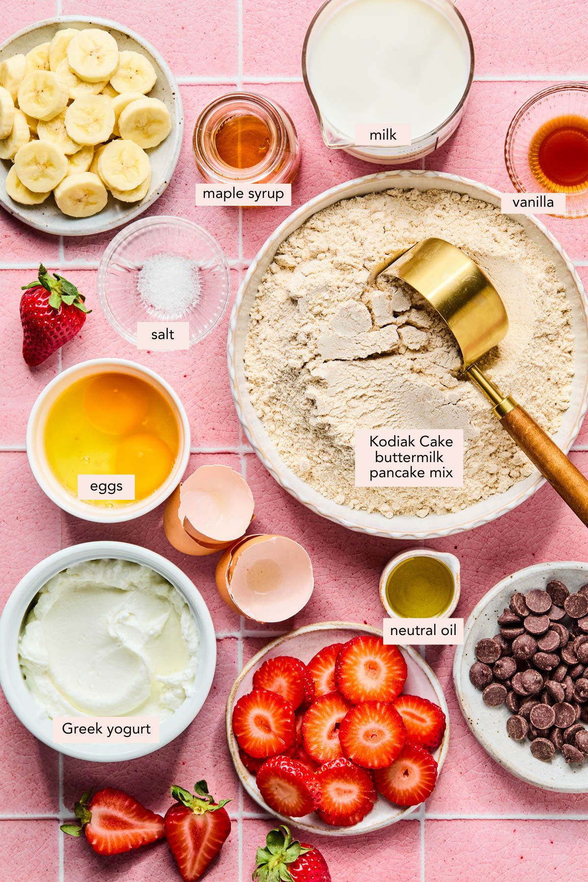 All of the ingredients for kodiak sheet pan pancakes in bowls on a pink countertop.