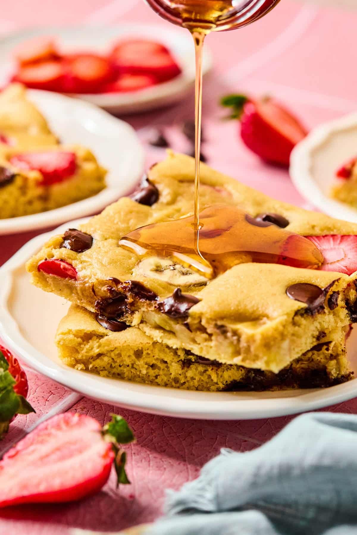 Two pieces of sheet pan pancakes on a white place with a drizzle of maple syrup on the top.