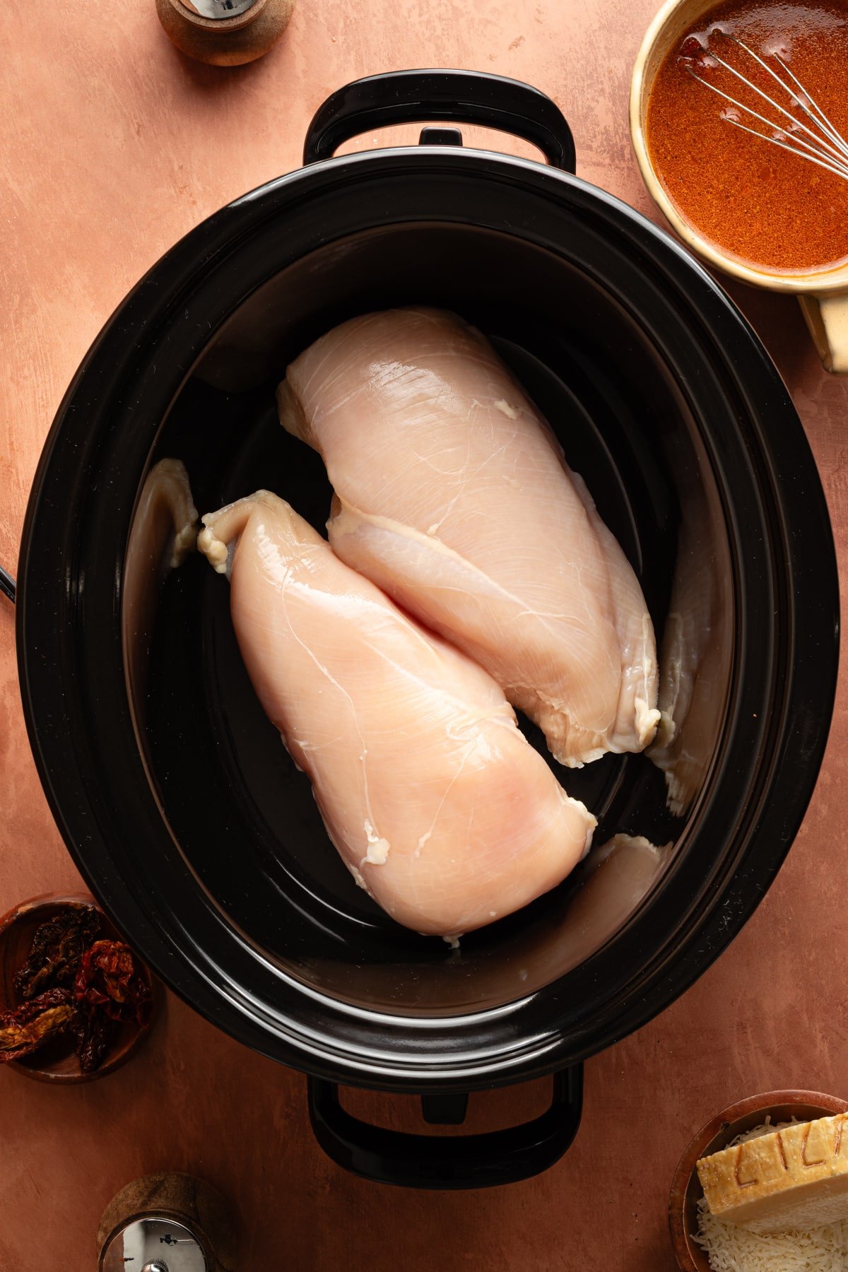 Two uncooked chicken breasts in the bottom of a slow cooker.