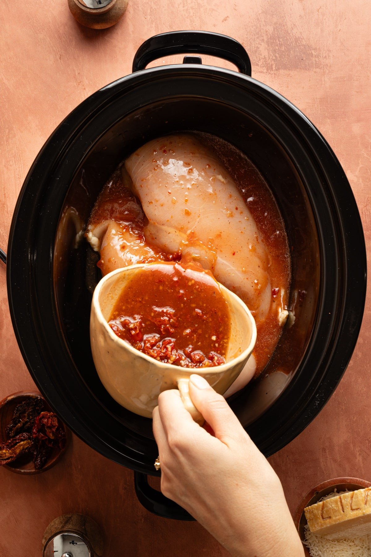 Pouring the chicken, garlic, tomato, salt, and pepper mixture over the chicken in the slow cooker.