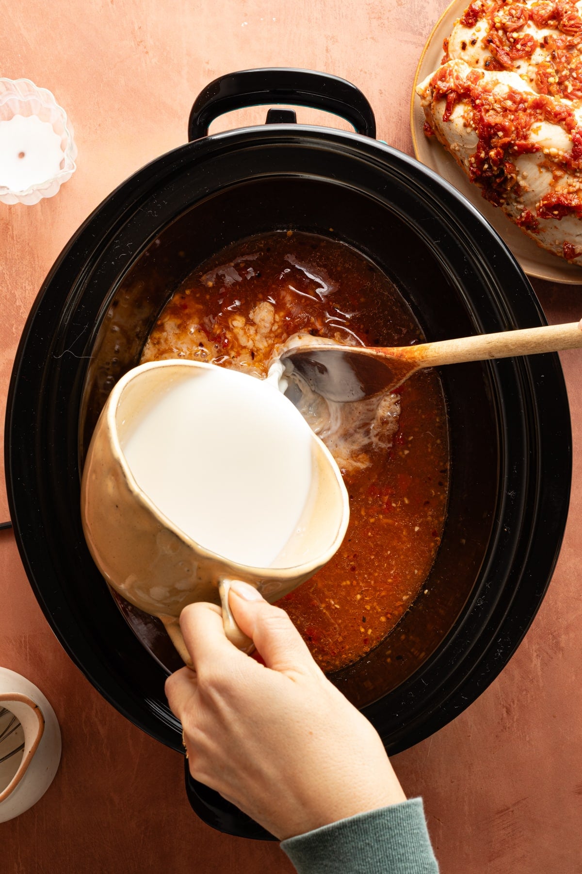Pouring the cream sauce into the slow cooker with the tomato broth mixture.