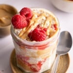 The peanut butter and jelly overnight oats in a jar for serving. A drizzle of peanut butter and three fresh raspberries sits on top of the oats.