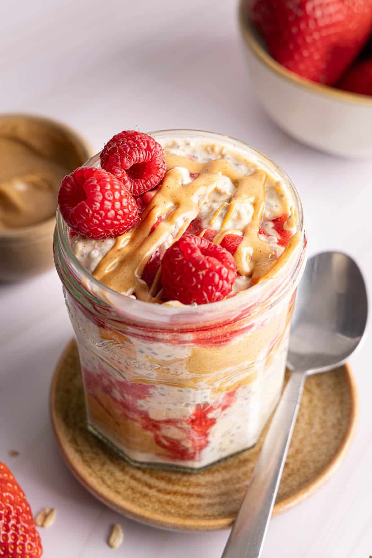 The peanut butter and jelly overnight oats in a jar for serving. A drizzle of peanut butter and three fresh raspberries sits on top of the oats.