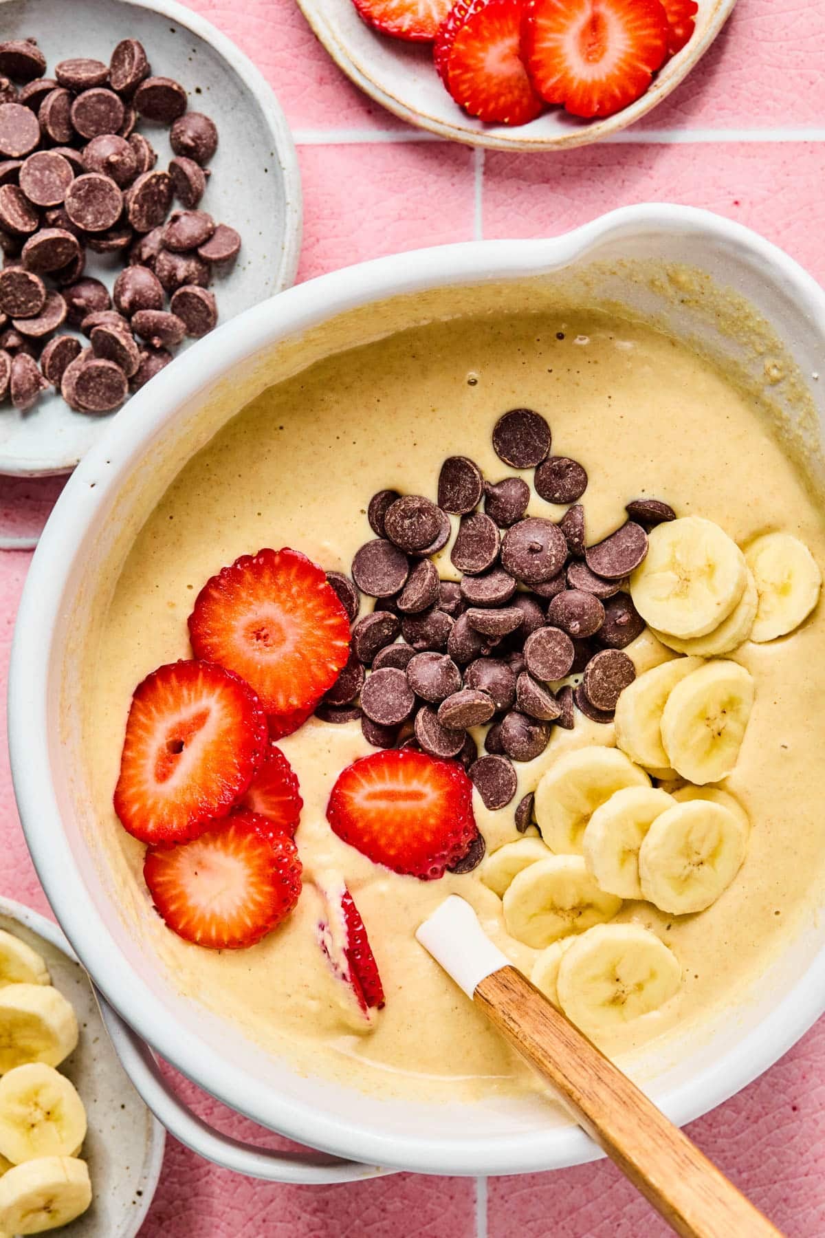 The add-ins of strawberries, chocolate chips and banana slices on top of the pancake batter in the bowl before stirring together.