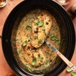 A serving spoon lifts a piece of slow cooker marry me chicken from the crockpot for serving.