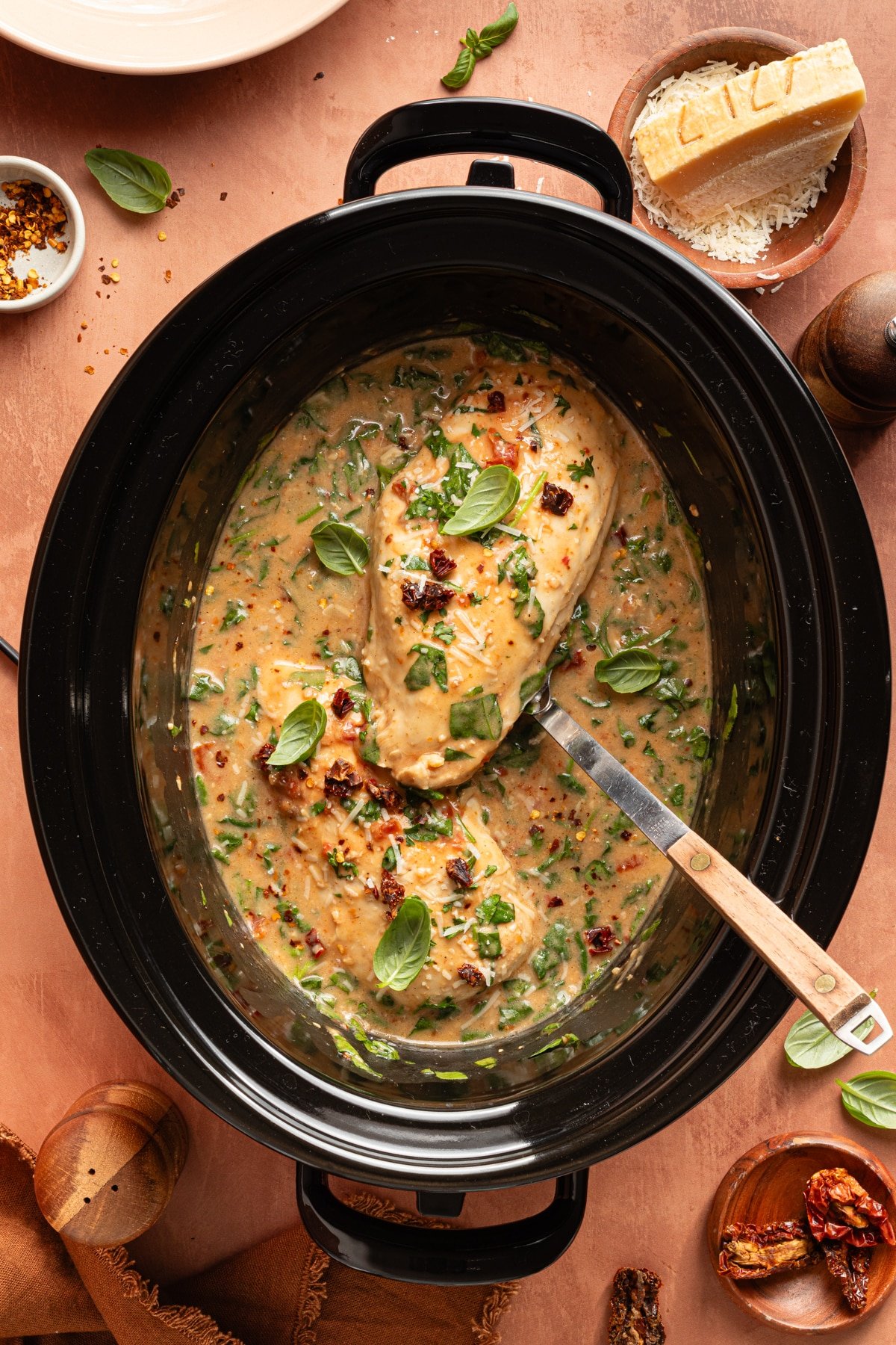 A serving spoon lifts a piece of slow cooker marry me chicken from the crockpot for serving.