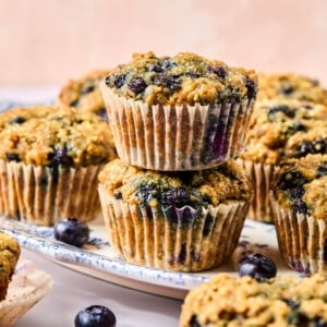 Two banana blueberry oatmeal muffins stacked on top of each other on a white dish on a countertop.