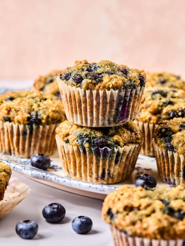 Two banana blueberry oatmeal muffins stacked on top of each other on a white dish on a countertop.