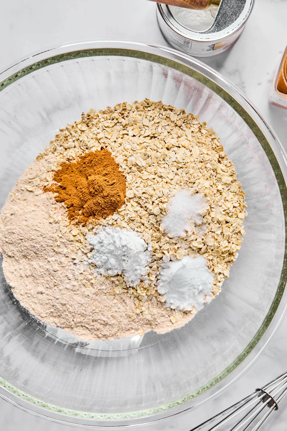 The dry ingredients for the banana blueberry oatmeal muffins in a glass bowl on a white countertop.