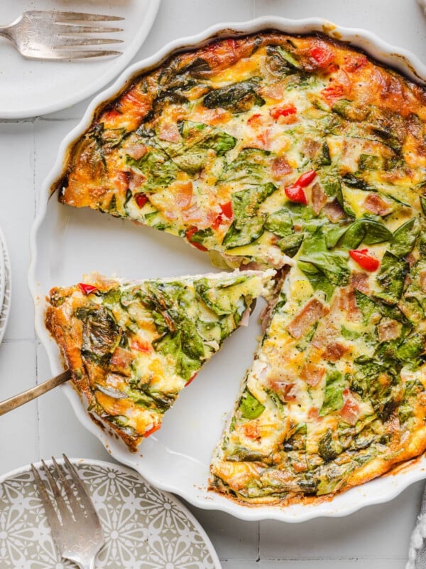 A serving utensil picking up a slice of crustless cottage cheese quiche from the baking dish.