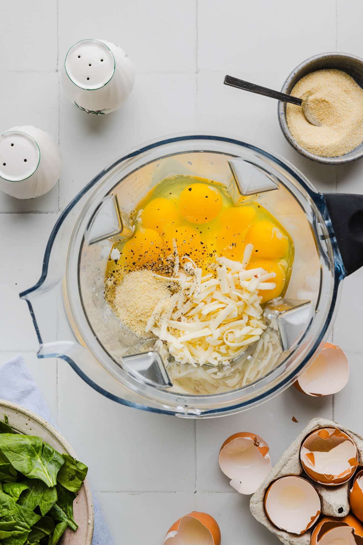 A blender filled with eggs, cottage cheese, cheddar cheese, onion powder, garlic powder and black pepper before blending.