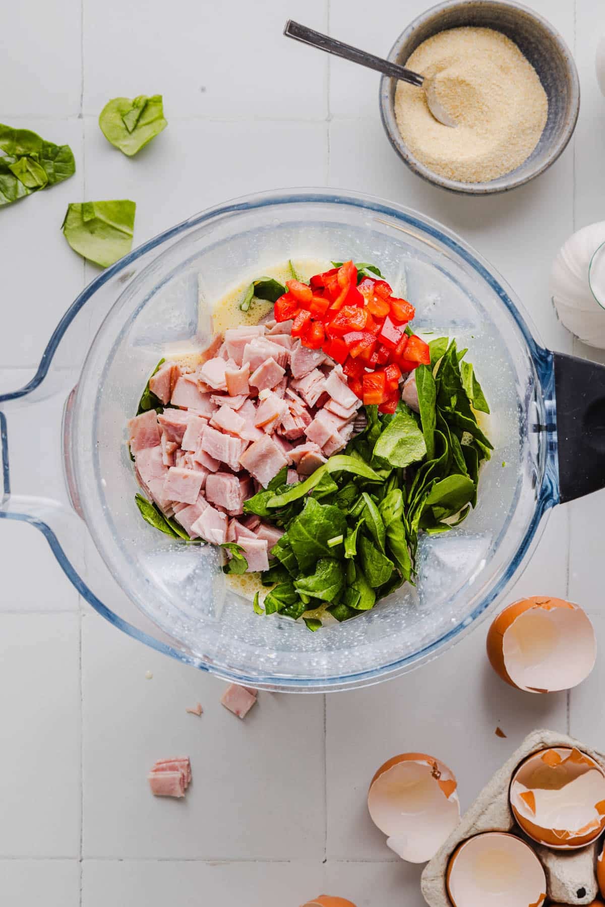 The ham, peppers, and spinach on top of the blended egg mixture in a blender before stirring together.