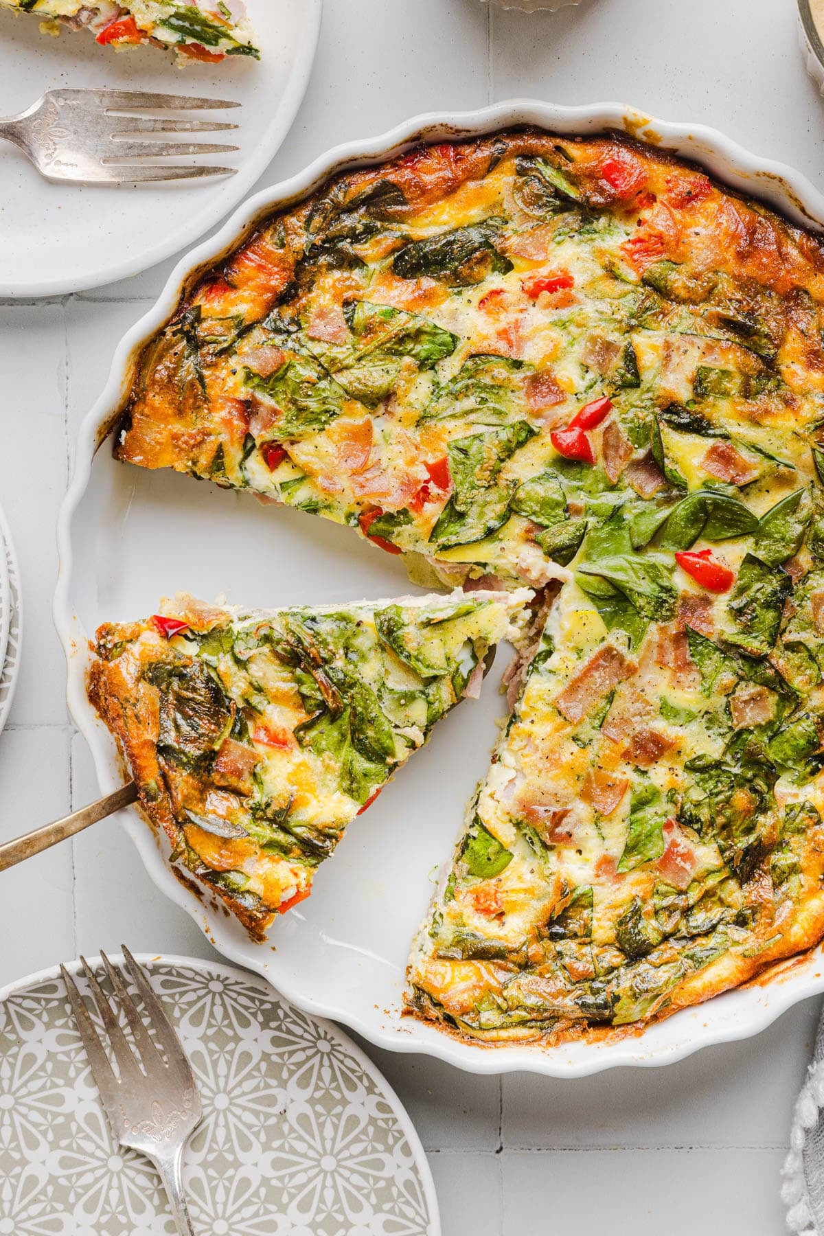 A serving spatula picking up a slice of crustless cottage cheese quiche from the baking dish.