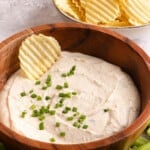 A wooden bowl filled with greek yogurt french onion dip with chopped chives.