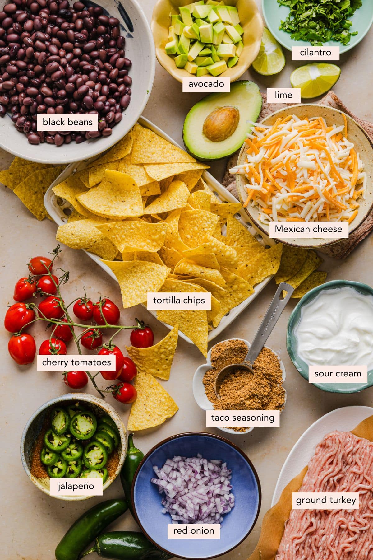 All of the ingredients for ground turkey nachos in bowls or a plate on a countertop.