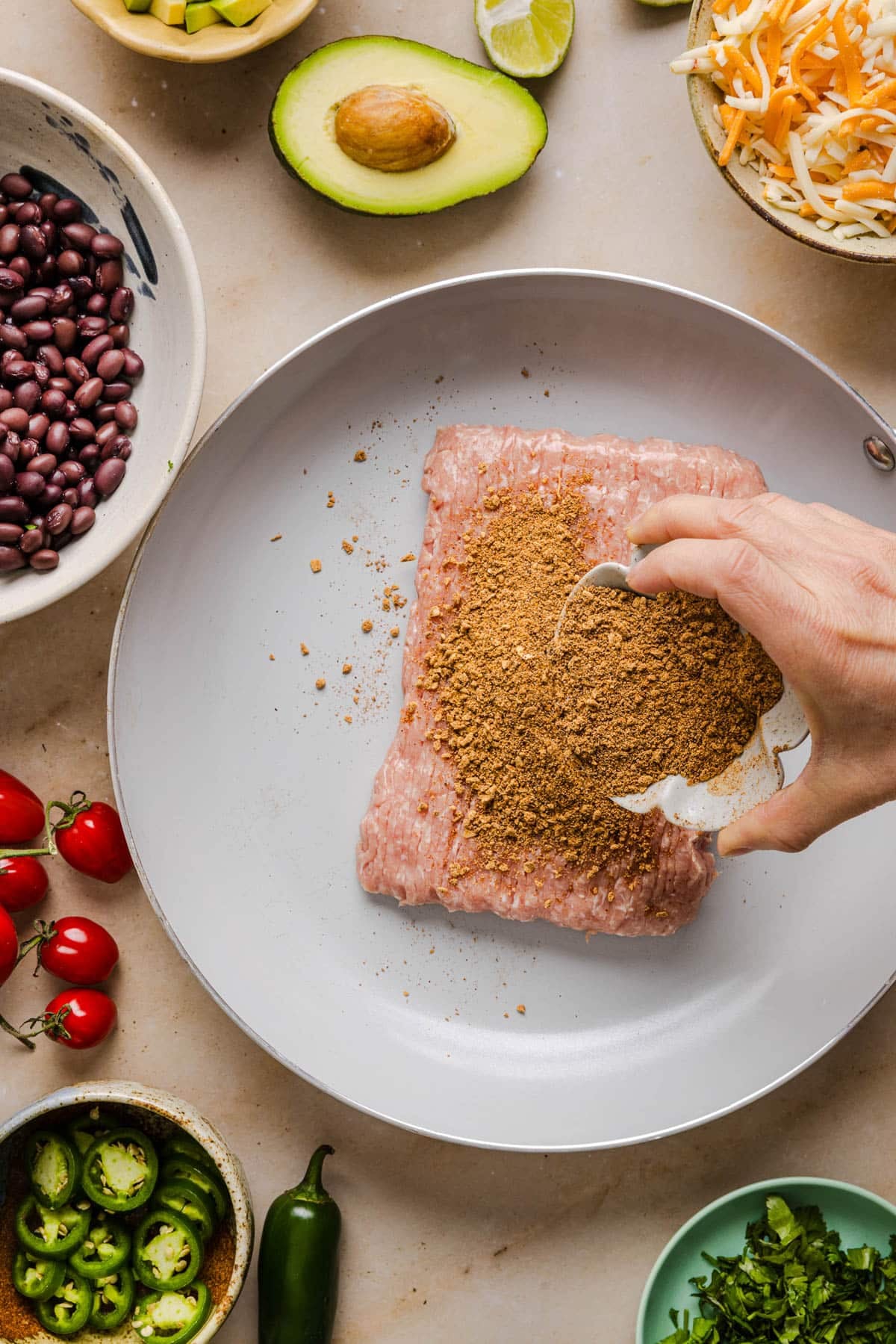 Sprinkling taco seasoning over the ground turkey in a skillet before cooking.