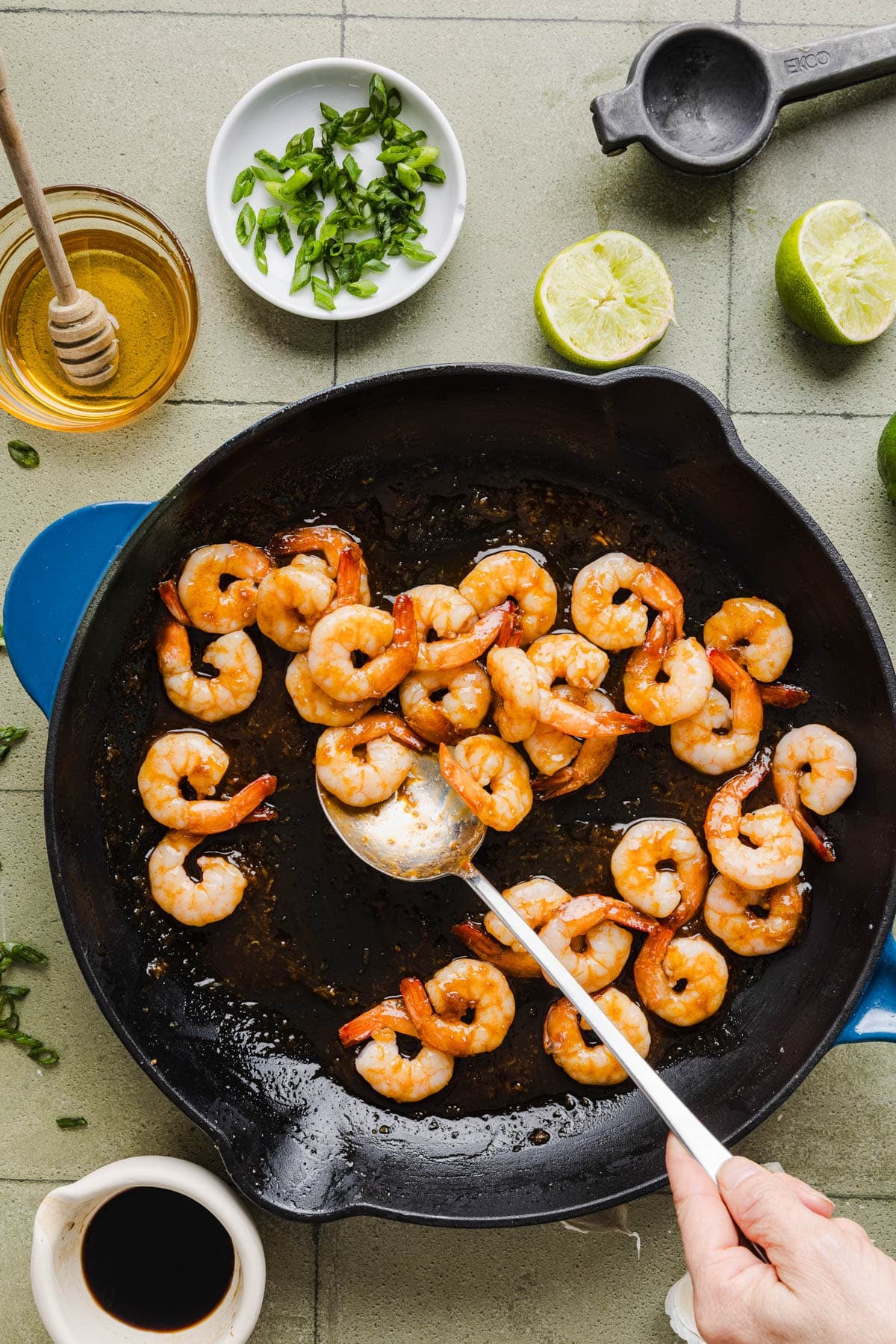 A hand holds a spoon tossing shrimp in the pan to coat in the sauce.