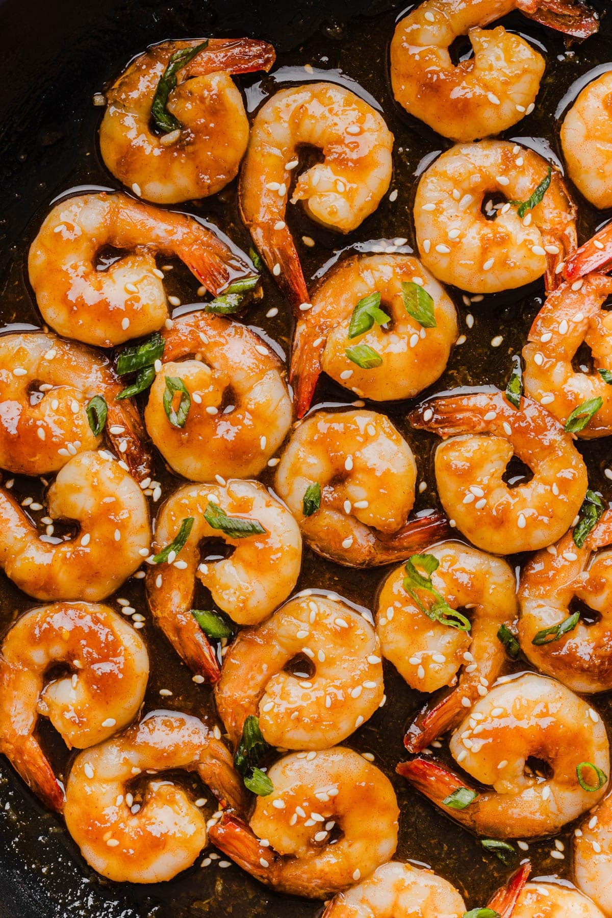 The cooked honey sriracha shrimp in the pan garnished with sliced green onions.