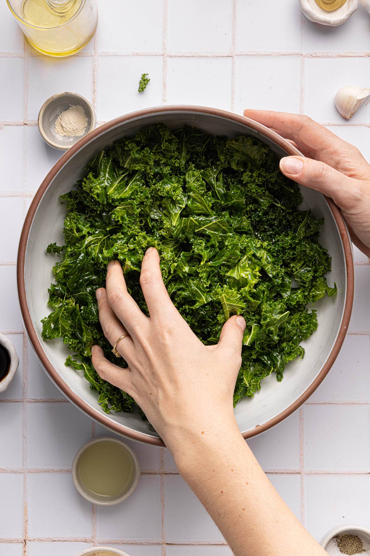 A hand massages the kale in a large bowl.