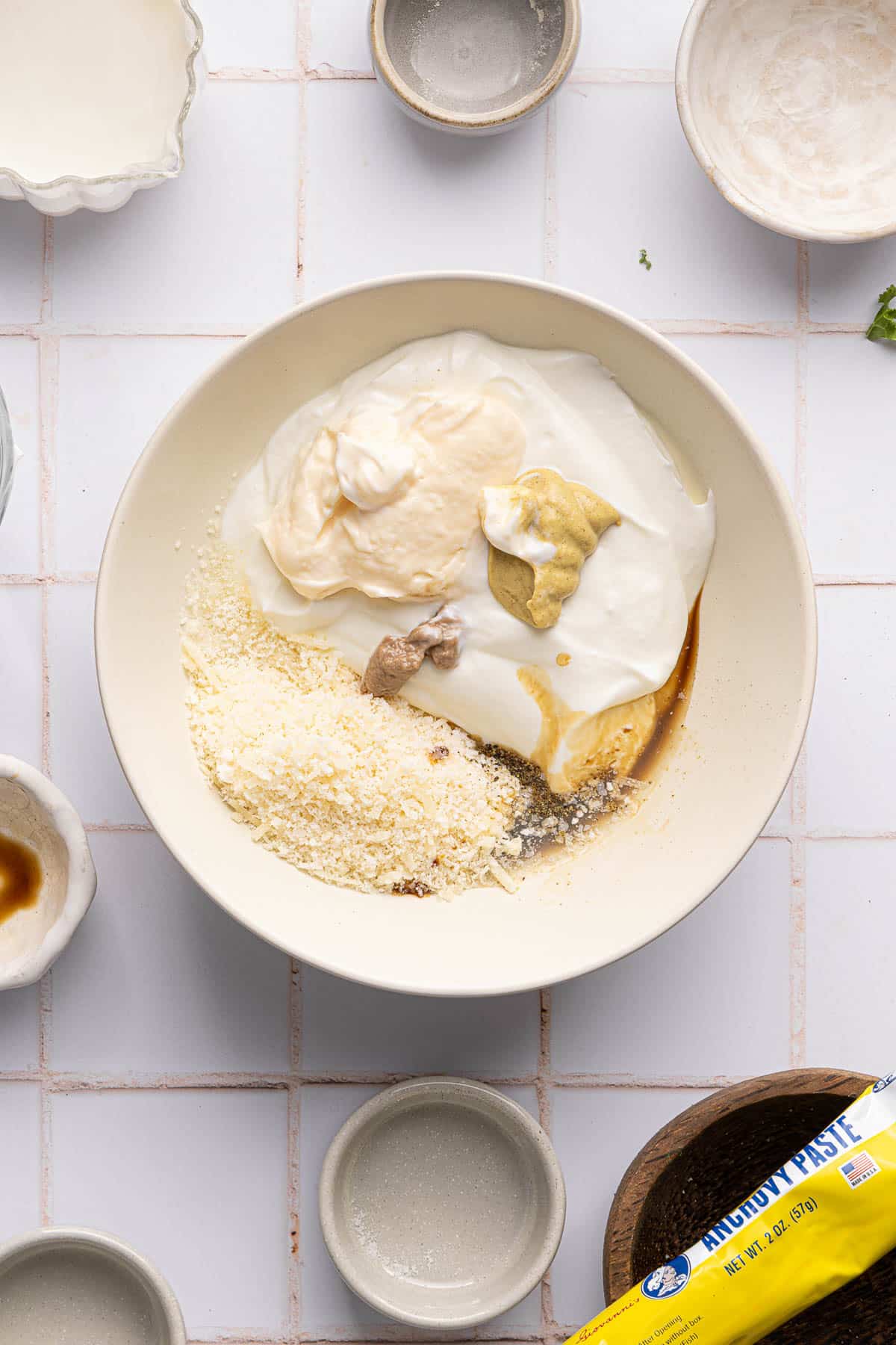 All of the ingredients for the Caesar dressing in a small white bowl before stirring together.