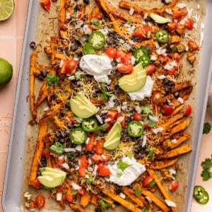 The baked loaded sweet potato fries on a baking sheet after baking with the fresh toppings like pico, sliced avocado, sliced jalapenos, and greek yogurt on top.