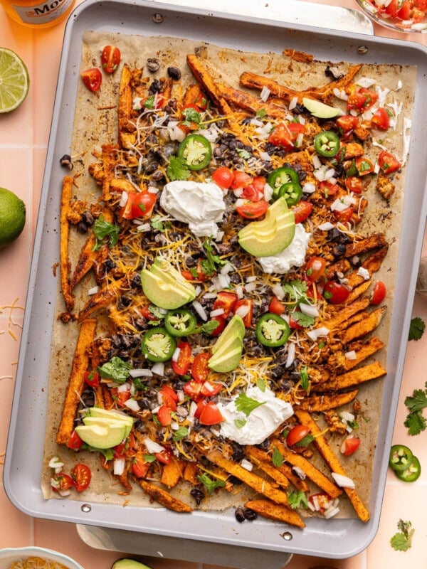 The baked loaded sweet potato fries on a baking sheet after baking with the fresh toppings like pico, sliced avocado, sliced jalapenos, and greek yogurt on top.