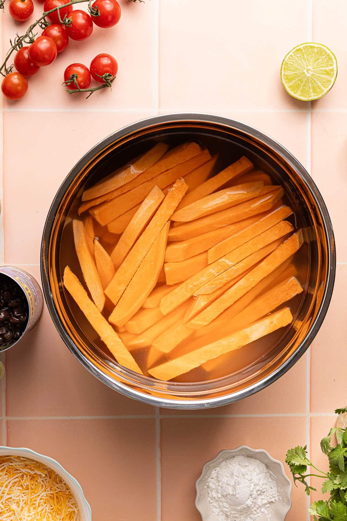 Cut sweet potato wedges in a bowl of water on a countertop.