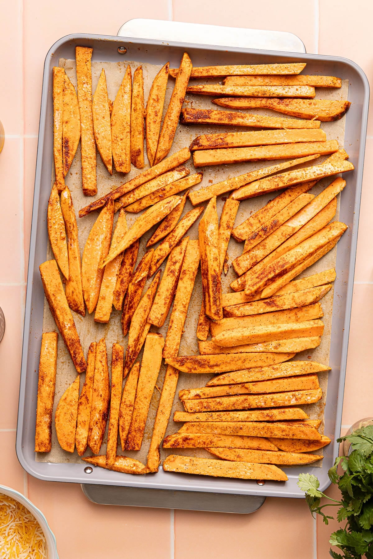 The coated sweet potatoes in an even layer on a baking sheet lined with parchment paper.