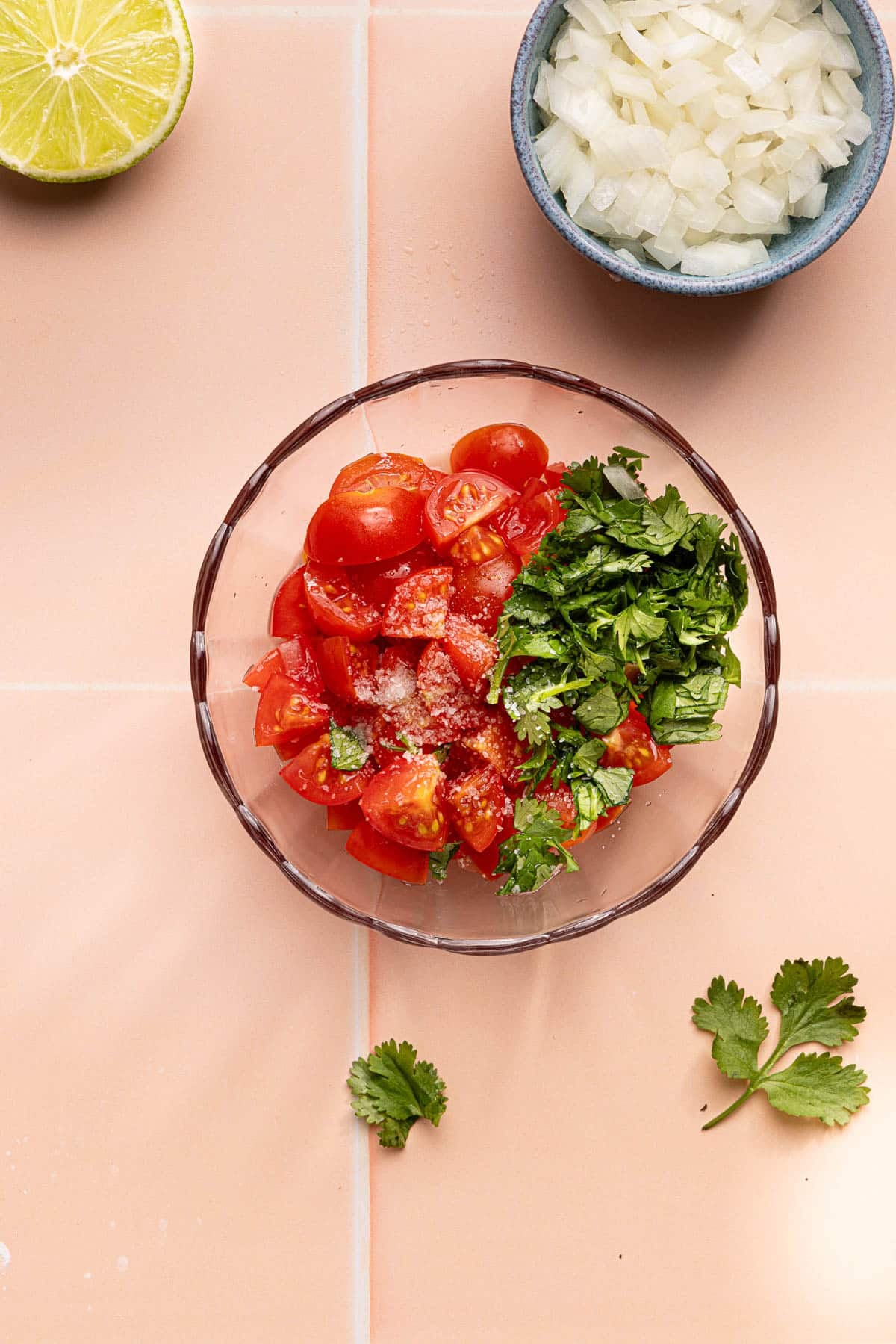 The quartered cherry tomatoes, diced onion, chopped cilantro, lime juice, and salt in a glass bowl on a countertop.