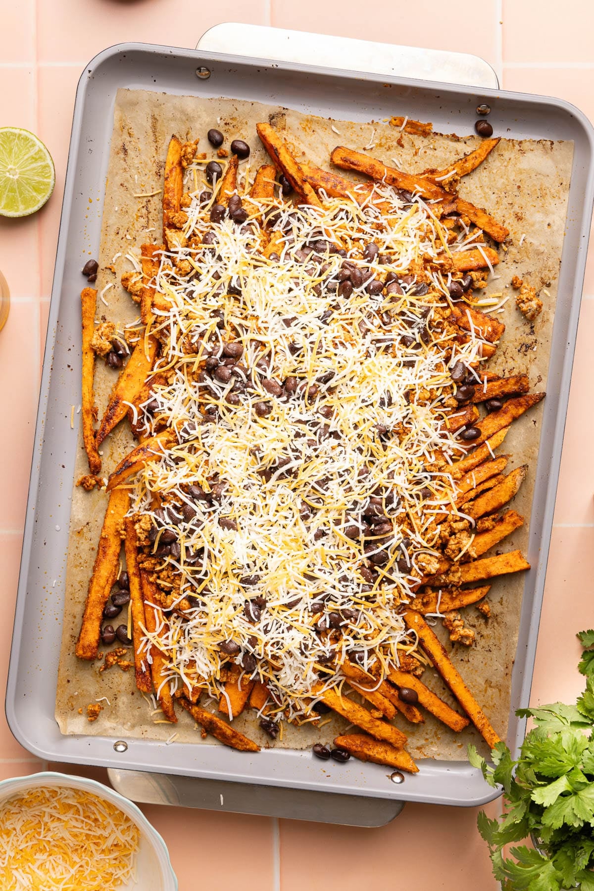 The baked sweet potato fries on a baking sheet with the cooked ground turkey, beans, and shredded cheese on top before going into the oven.