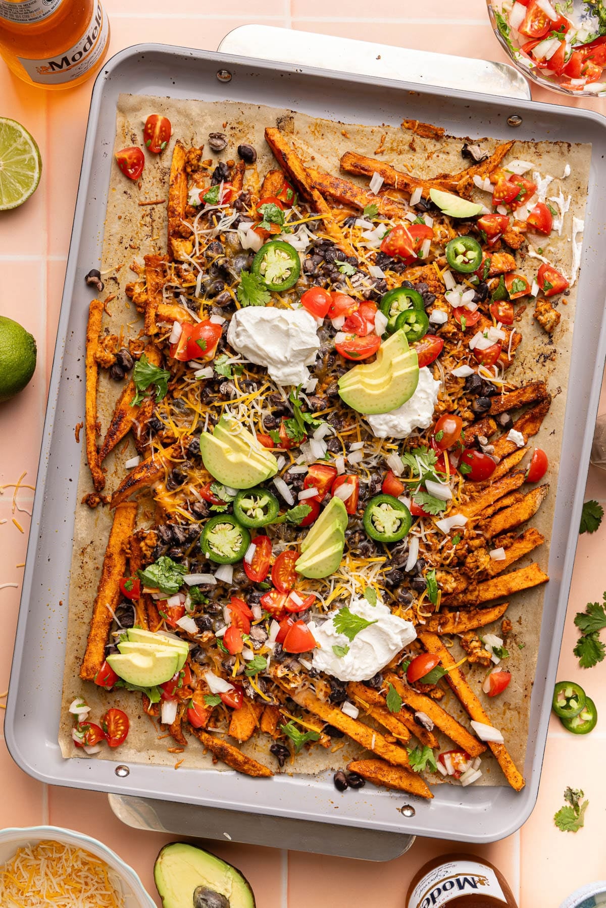 The baked loaded sweet potato fries on a baking sheet after baking with the fresh toppings like pico, sliced avocado, sliced jalapenos, and greek yogurt on top.