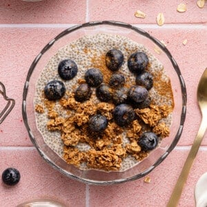 Chia oat milk pudding in a glass bowl topped with granola and fresh blueberries.