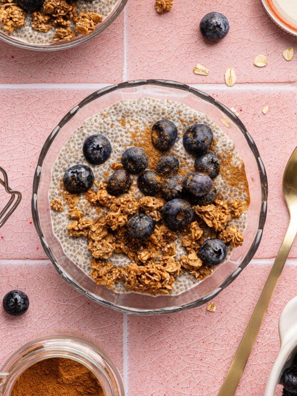 Chia oat milk pudding in a glass bowl topped with granola and fresh blueberries.