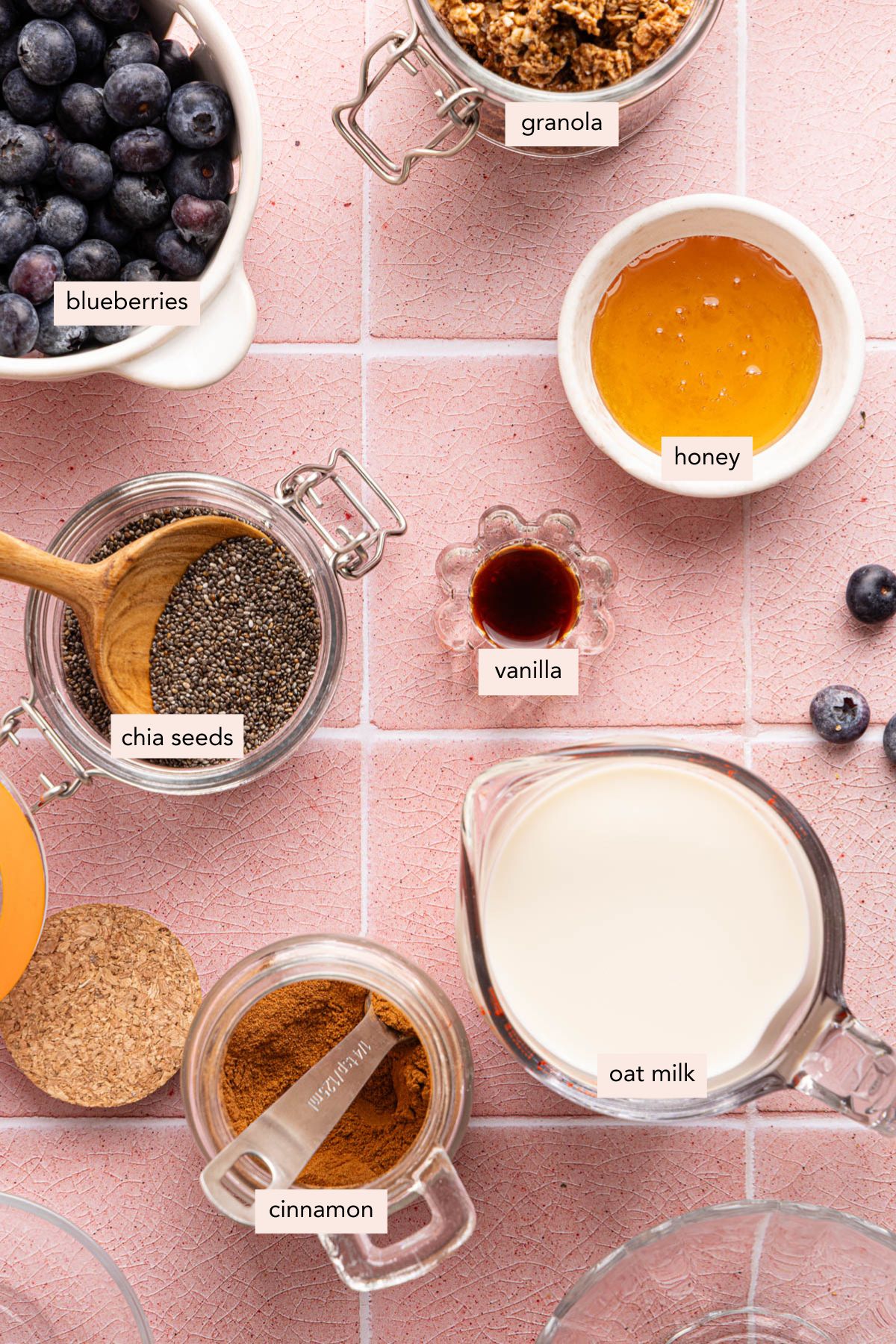 All of the ingredients for the oat milk chia pudding in bowls on a pink tile countertop.